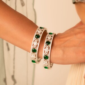May include: A pair of silver bangles with green emerald stones and white cubic zirconia stones.