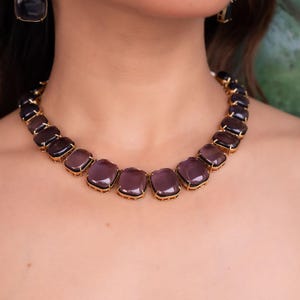 May include: A gold necklace with a row of large, square, purple stones.