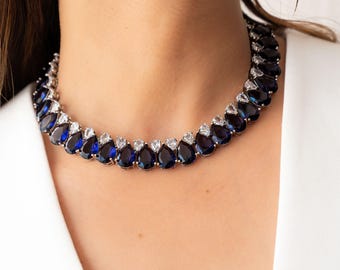 May include: A silver choker necklace with a graduated design of teardrop-shaped blue and clear rhinestones.