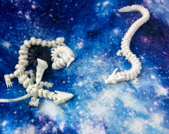 May include: Two white articulated dragon skeletons on a blue and white galaxy print fabric. The dragons are posed in a confrontational stance.