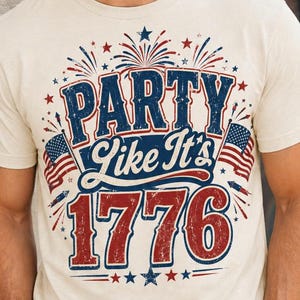 May include: Cream-colored t-shirt with the text "PARTY like It's 1776" in red, white, and blue. The design includes fireworks, stars, and American flags. The shirt is short-sleeved.
