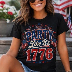 May include: Black t-shirt with the text "PARTY Like It's 1776" in red, white, and blue. The design includes fireworks and American flags, celebrating the spirit of the Fourth of July.