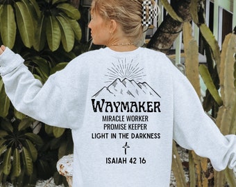 Op de afbeelding: Een grijs sweatshirt met een afbeelding van bergen en de tekst "Waymaker, Miracle Worker, Promise Keeper, Light in the Darkness, Isaiah 42:16".