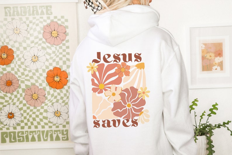 May include: White hoodie featuring a floral design and the words "Jesus saves" in brown lettering. The design includes peach, orange, and yellow flowers. A casual, comfortable garment.