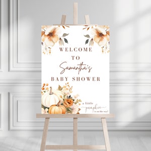 May include: Welcome to Samantha's Baby Shower sign with a fall theme. The sign features a white background with brown text and a watercolor illustration of pumpkins and flowers.