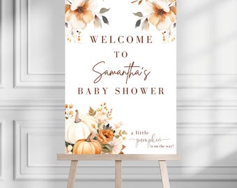May include: A welcome sign for Samantha's baby shower, displayed on a wooden easel. The sign features floral watercolor designs in shades of orange and brown, with pumpkins and the phrase "a little pumpkin is on the way!"