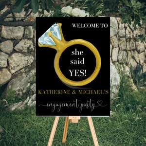 May include: Black and gold engagement party sign with a diamond ring illustration. The sign reads "Welcome to she said YES! Katherine & Michael's engagement party".