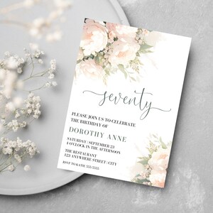 Op de afbeelding: Een witte uitnodigingskaart met een bloemenontwerp in roze en groene tinten. De tekst op de kaart luidt "zeventig" en bevat details voor een verjaardagsfeest voor Dorothy Anne.