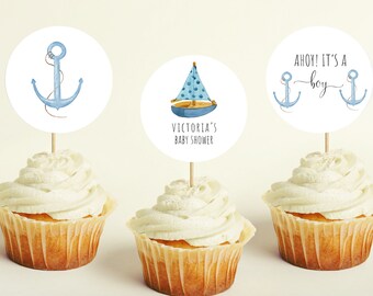Puede incluir: Tres adornos para cupcakes con temas náuticos. El primer adorno presenta un ancla azul con una cuerda. El segundo adorno presenta un velero azul y blanco. El tercer adorno presenta dos anclas azules y el texto "Ahoy! It's a boy".