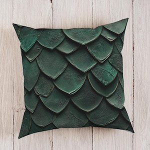 May include: Square decorative pillow with a dark green, textured, overlapping scale pattern. The pillow has a slightly distressed appearance, with variations in the green color. The pillow is a home decor item.