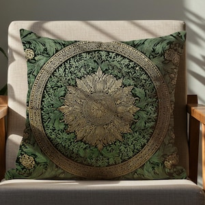 Puede incluir: Cojín decorativo verde y dorado con un diseño floral, colocado sobre una silla de madera. El cojín presenta un diseño central de sol dentro de un borde circular. La habitación está decorada con plantas y luz natural.