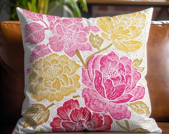 May include: A decorative throw pillow with a floral pattern. The pillow features large, stylized flowers in shades of pink, yellow, and red against a white background. The pillow is square and rests on a brown leather couch.