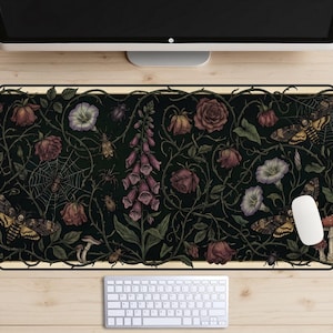 Op de afbeelding: Decoratieve bureaumat met een donkergroene achtergrond en een bloemen- en insectenontwerp. Het ontwerp bevat rozen, motten, spinnen en andere botanische elementen. Een witte muis en toetsenbord zijn zichtbaar.