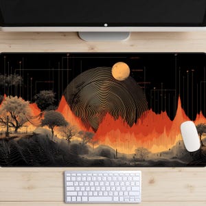 Puede incluir: Alfombrilla de ratón rectangular negra con un diseño de paisaje con árboles, montañas y un sol. El diseño incorpora tonos de naranja, amarillo y negro. Un ratón y un teclado blancos son visibles debajo.