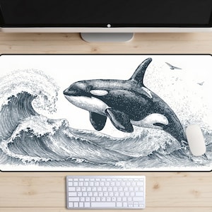 May include: A white rectangular mousepad featuring a detailed black and white illustration of a killer whale leaping out of ocean waves. The design includes seagulls and water splashes, with a white mouse and keyboard visible.