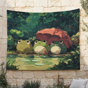May include: A tapestry featuring an illustration of three cartoon frogs under an orange umbrella in a rainy forest scene. The frogs are green and white, and the background is a lush green with water and lily pads.