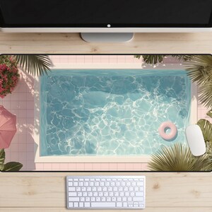 以下が含まれることがあります： プールシーンが描かれた長方形のデスクマット。ピンクの浮き輪が水面に浮かんでいます。マットはピンクの縁取り、白いキーボードとマウス、ヤシの葉が特徴です。夏の休暇のシーンです。