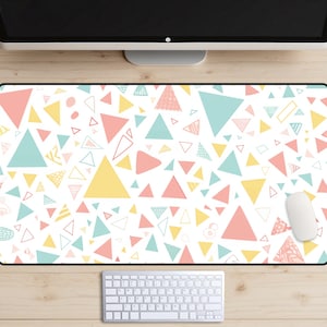 May include: A white desk mat with a repeating pattern of pink, yellow, and blue triangles. The mat is on a wooden desk with a computer monitor, keyboard, and mouse.