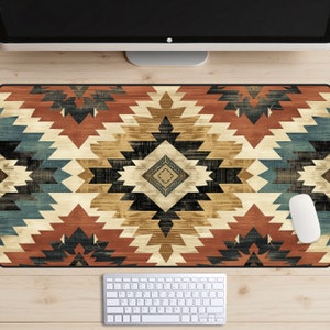 Puede incluir: Una alfombrilla de escritorio con estampado geométrico de colores con un diseño en negro, marrón, rojo, azul y beige. La alfombrilla está sobre una superficie de madera con un teclado y un ratón blanco.