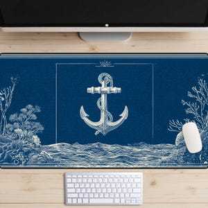 Può includere: Un tappetino da scrivania blu navy con un design di ancora nautica bianca. Il tappetino è rettangolare e include una tastiera e un mouse bianchi. Il design incorpora onde oceaniche ed elementi botanici.