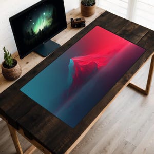 Pode incluir: Um tapete de rato preto com um design abstrato de paisagem de montanha azul e vermelho. O tapete de rato está sobre uma mesa de madeira com um monitor de computador e outros itens.