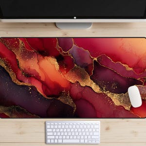 May include: A rectangular desk mat with a vibrant abstract design in shades of red, orange, and purple, accented with gold flecks. A white mouse and keyboard are visible on a wooden surface.