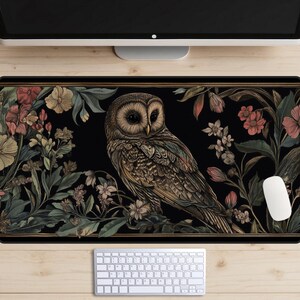 May include: A black and gold mouse mat featuring a detailed illustration of an owl perched on a branch with floral accents. The owl is brown and gold with a white face and black eyes.