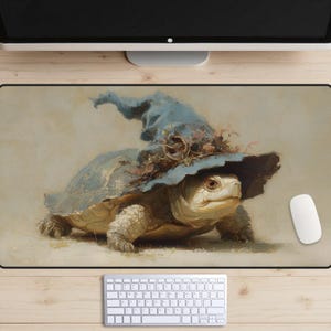 May include: A whimsical mousepad featuring a turtle wearing a blue witch's hat adorned with leaves. The turtle has a light-coloured shell and is set against a neutral background. A white mouse and keyboard are visible.