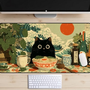 May include: A black cat with large eyes sits in front of a bowl of ramen on a decorative mousepad. The mousepad features a Japanese-style wave and sun design, with a cup, bottles, and a spoon.