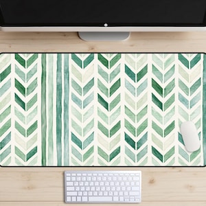 Op de afbeelding: Een rechthoekige bureaumat met een aquarelpatroon van verticale kolommen met afwisselende groene en lichtgroene chevronvormen, afgewisseld met dunne verticale strepen in verschillende tinten groen op een crèmekleurige achtergrond.