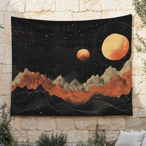 May include: A black tapestry with an orange and gold celestial design. The artwork features two large orange planets, a mountain range, and a starry night sky. The tapestry is hanging on a stone wall.