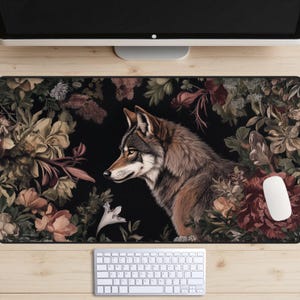 May include: A dark floral patterned mousepad with a wolf illustration in the center. The wolf is looking to the left and is surrounded by flowers in shades of pink, white, and green.