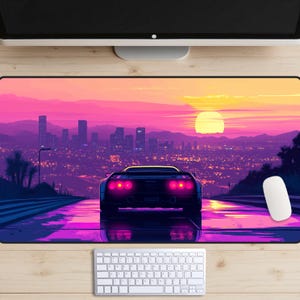 May include: A black sports car drives down a road with a city skyline in the background. The sky is a vibrant pink and orange with a large yellow sun setting in the distance.