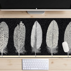 May include: Black and white desk mat with a repeating pattern of five stylised feathers. The feathers have a black and white striped pattern.