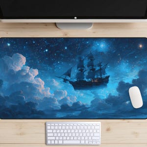 Puede incluir: Alfombrilla de ratón rectangular con una escena de fantasía de un velero flotando en un cielo nocturno estrellado. El barco es oscuro, con velas ondeantes, sobre un fondo de nubes azules y una galaxia brillante. Se ven un ratón y un teclado blancos.