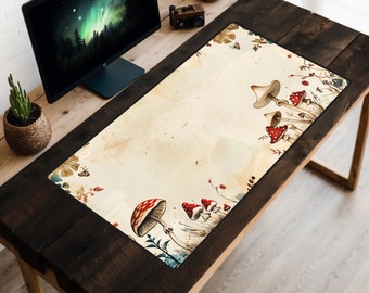 May include: A brown wooden desk with a black and white desk mat featuring a vintage style illustration of red and white mushrooms with green leaves and stems. The desk mat is on a wooden desk with a computer monitor and a potted plant.