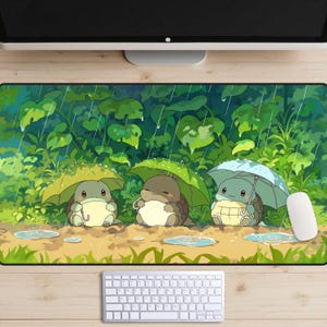 May include: A rectangular mouse mat with an illustration of three cartoon turtles under umbrellas in a rainstorm. The background shows green foliage and raindrops. A white mouse and keyboard are visible.