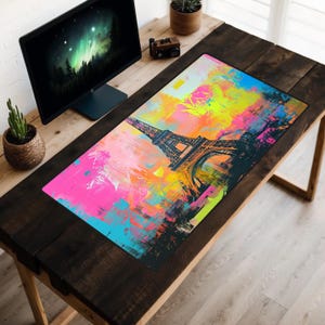 May include: A colorful desk mat with a graphic of the Eiffel Tower in Paris, France. The mat is on a wooden desk with a computer monitor and a potted plant.