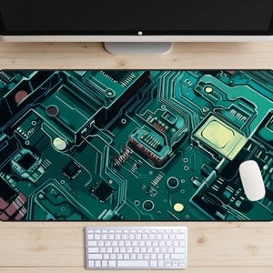 Pode incluir: Um rato, teclado e monitor de computador estão numa secretária de madeira. O foco está numa grande almofada de rato retangular com um design detalhado de placa de circuito em tons de verde, verde-azulado e amarelo. A almofada do rato é o elemento central.