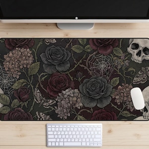 Puede incluir: Alfombrilla de ratón decorativa con un diseño floral oscuro con rosas, hortensias y polillas. La paleta de colores incluye tonos de gris, burdeos y negro. También se incorporan calaveras y telarañas. Se ve un ratón y un teclado blancos.