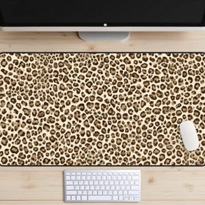 Peut inclure: Un tapis de bureau rectangulaire avec un motif léopard dans les tons marron et beige. Une souris et un clavier d'ordinateur blancs sont visibles sur le bureau en bois. Le tapis est conçu pour protéger la surface du bureau.