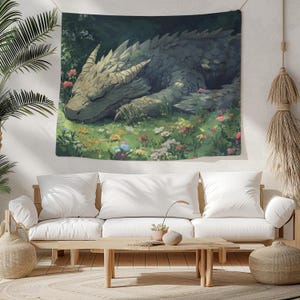 May include: A tapestry featuring a green, brown, and gray dragon sleeping in a field of colorful flowers. The dragon has a long snout and large, scaly wings.