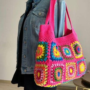 Peut inclure: Un sac cabas en crochet rose vif avec des carrés de grand-mère colorés. Le sac a une base large et plate et deux longues anses.