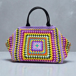 Puede incluir: Bolso tote de ganchillo colorido con diseño de granny square. El bolso presenta una vibrante mezcla de colores como morado, amarillo, naranja y verde. Tiene asas negras y una forma rectangular.