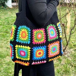 May include: A black crochet tote bag with colorful granny squares. The squares feature a variety of colors, including red, orange, yellow, green, blue, and purple.