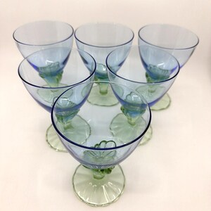 K&ouml;nnte beinhalten: Sechs Vintage-Gl&auml;ser mit blauem und gr&uuml;nem Stiel. Die Gl&auml;ser haben eine abgerundete Schalenform mit blauem Farbton und einen gr&uuml;nen Stiel und Fu&szlig;. Der Stiel weist ein Blumendesign auf. Die Gl&auml;ser sind kreisf&ouml;rmig angeordnet.