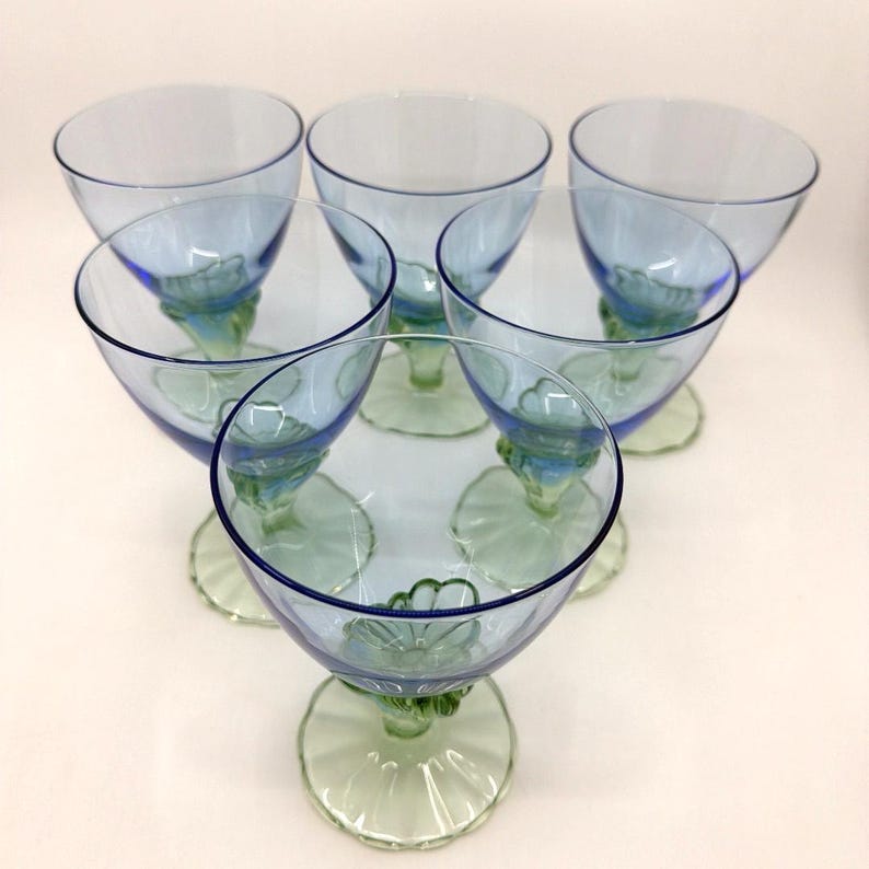 K&ouml;nnte beinhalten: Sechs Vintage-Gl&auml;ser mit blauem und gr&uuml;nem Stiel. Die Gl&auml;ser haben eine abgerundete Schalenform mit blauem Farbton und einen gr&uuml;nen Stiel und Fu&szlig;. Der Stiel weist ein Blumendesign auf. Die Gl&auml;ser sind kreisf&ouml;rmig angeordnet.