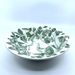 May include: White ceramic serving bowl with a green botanical design featuring various vegetables and foliage. The bowl has a wide, shallow shape, suitable for salads or side dishes. The design includes tomatoes, beans, and artichokes.