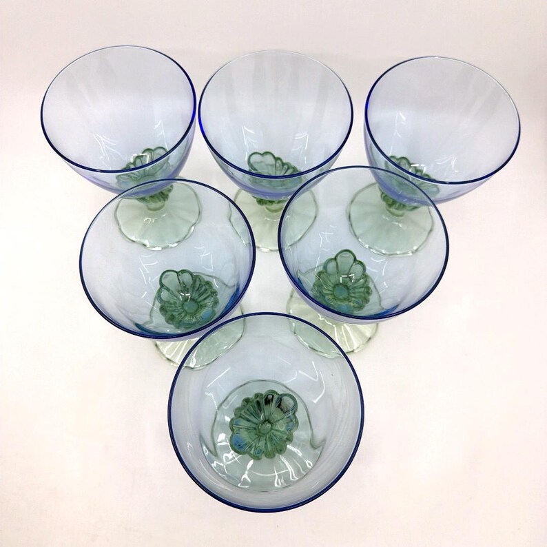 K&ouml;nnte beinhalten: Sechs transparente Weingl&auml;ser mit blauem Rand und gr&uuml;nem Blumendesign am Boden. Die Gl&auml;ser sind kreisf&ouml;rmig angeordnet und pr&auml;sentieren ihr elegantes Design. Ideal zum Servieren von Getr&auml;nken bei einer besonderen Veranstaltung.