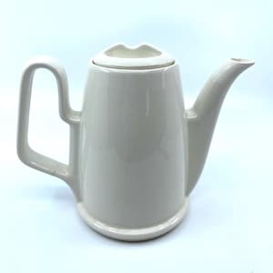 May include: Cream-colored ceramic teapot with a unique design. The teapot features a curved handle, a long spout, and a lid with a lip-shaped opening. The teapot has a glossy finish and a minimalist aesthetic, suitable for serving tea.